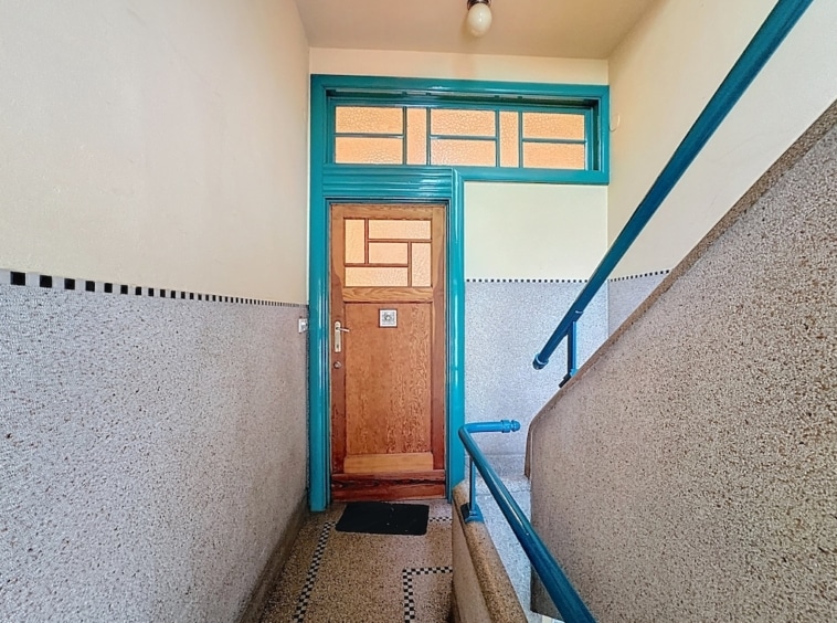 Escalier vintage menant à une porte en bois turquoise avec vitres géométriques et garde-corps assorti.