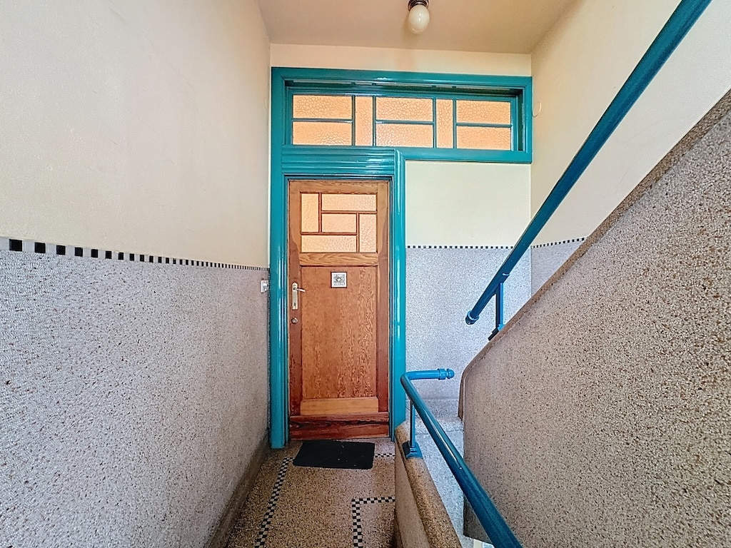Escalier vintage menant à une porte en bois turquoise avec vitres géométriques et garde-corps assorti.