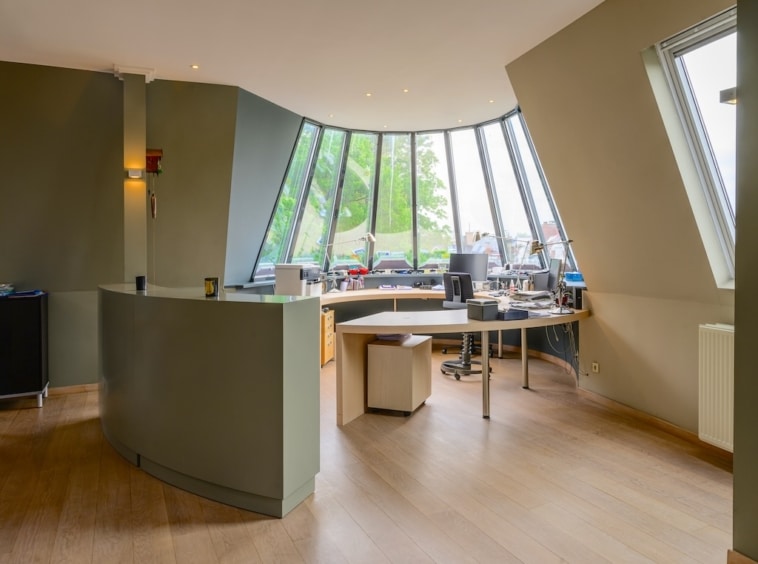 Bureau moderne avec murs courbes, grandes fenêtres lumineuses et espace collaboratif élégant.