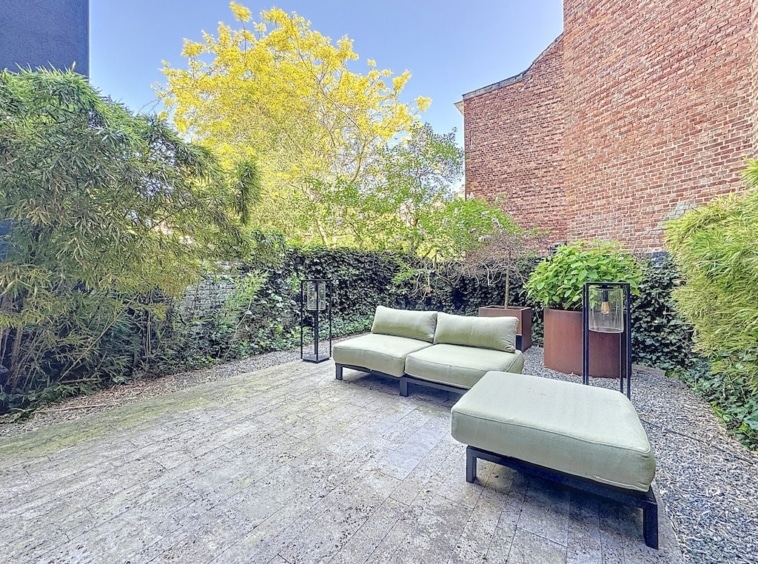 Espace extérieur lounge avec mobilier moderne, mur en briques, végétation et sol en galets.