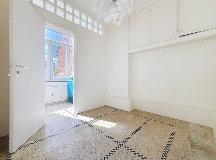 Salle moderne lumineuse avec sol clair, décoration géométrique, grande fenêtre et luminaire artistique.