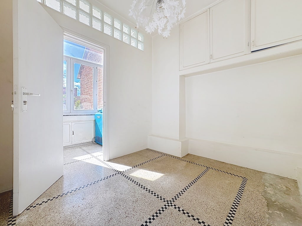 Salle moderne lumineuse avec sol clair, décoration géométrique, grande fenêtre et luminaire artistique.