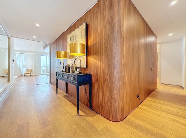 Couloir moderne en bois, lumineux, avec meuble noir, lampes dorées et œuvre artistique élégante.