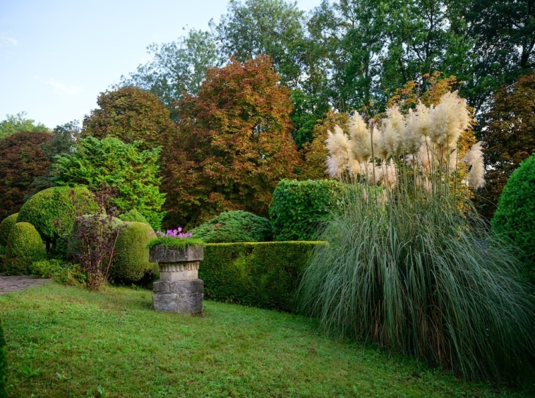 Jardin automnal paisible avec arbres colorés, buissons taillés et sculptures en pierre élégantes.