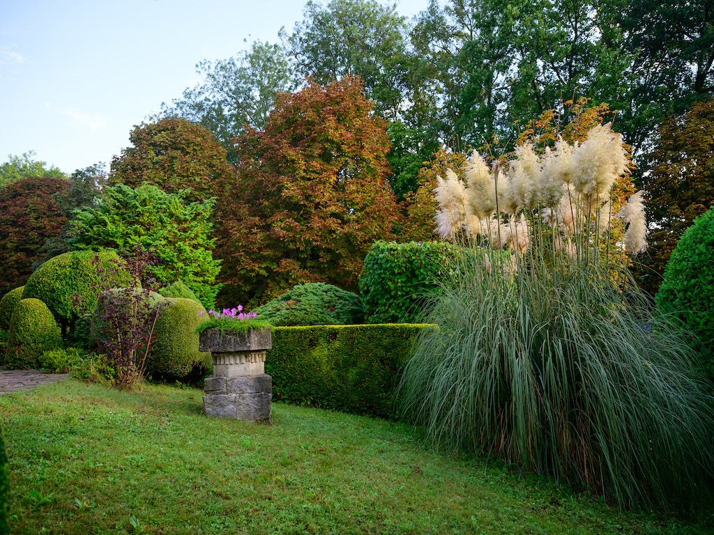 Jardin automnal paisible avec arbres colorés, buissons taillés et sculptures en pierre élégantes.