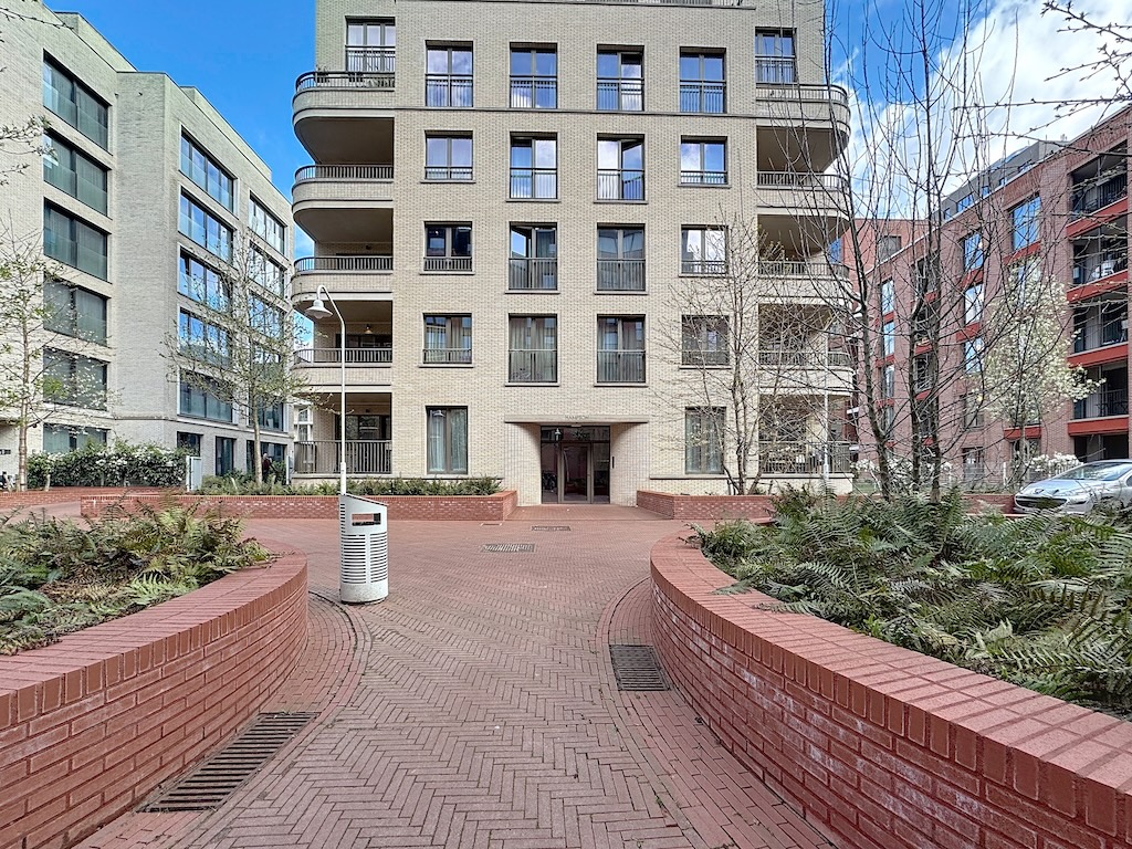 Résidence moderne avec jardins, chemins en briques, balcons lumineux, dans un cadre urbain verdoyant.