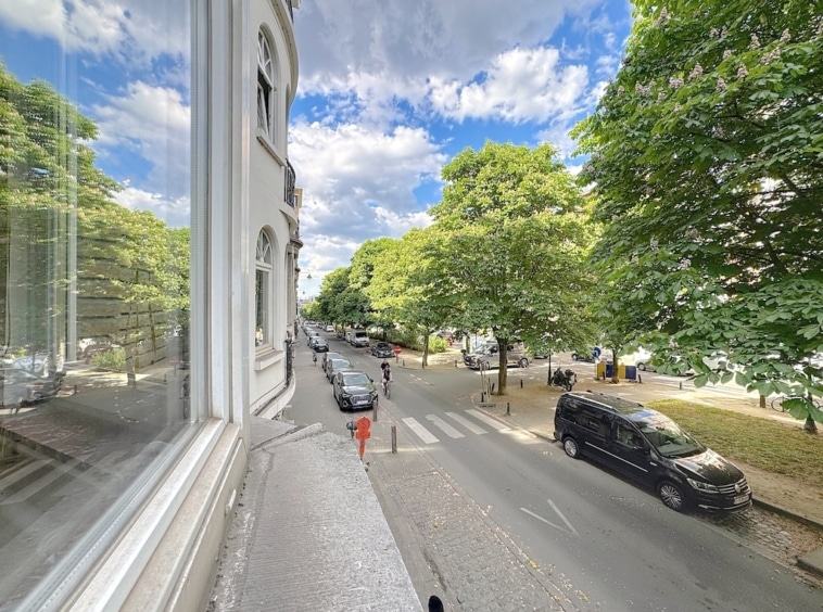 Rue pittoresque avec arbres, voitures et piéton en rouge sous un ciel bleu nuageux.