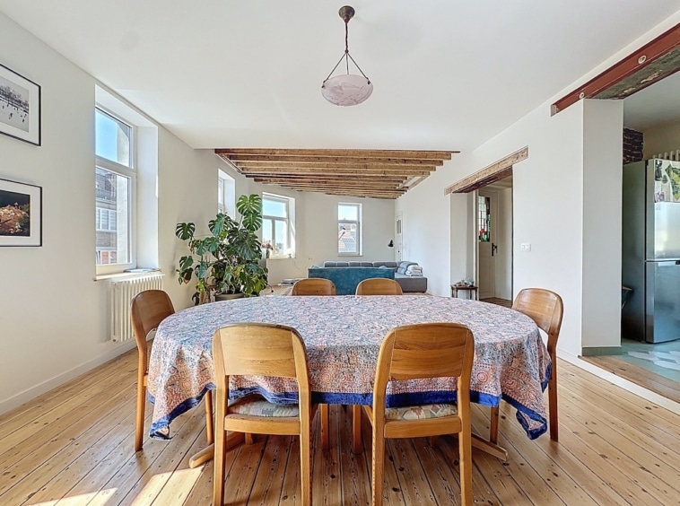 Salle à manger lumineuse avec table ronde, décor moderne, poutres en bois et vue ouverte.