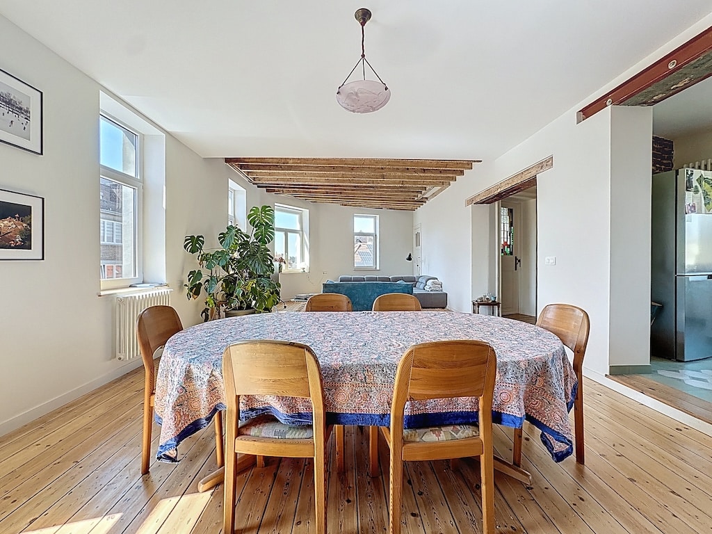Salle à manger lumineuse avec table ronde, décor moderne, poutres en bois et vue ouverte.