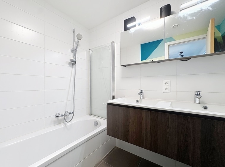 Salle de bain moderne avec double lavabo, baignoire, douche en verre, design épuré et élégant.
