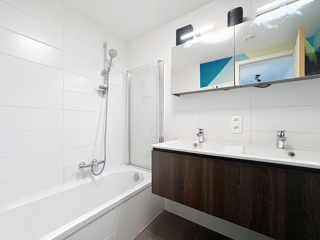 Salle de bain moderne avec double lavabo, baignoire, douche en verre, design épuré et élégant.