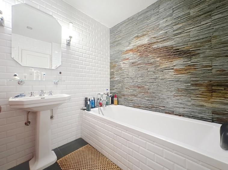 Salle de bain moderne avec mur en pierre, baignoire blanche élégante et accessoires design.
