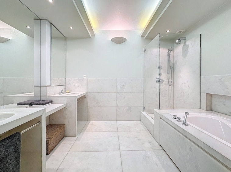 Salle de bain moderne épurée avec baignoire îlot, douche à l’italienne et éclairage chaleureux.