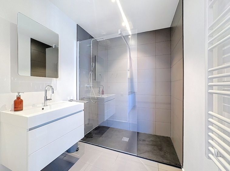 Salle de bain moderne, élégante, lumineuse avec douche à l’italienne, miroir carré et radiateur design.