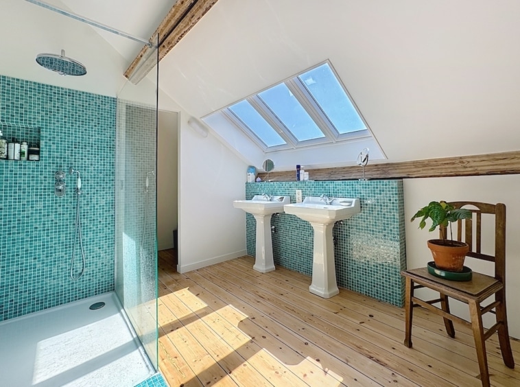 Salle de bain attique moderne avec murs turquoise, douche en verre et ambiance chaleureuse en bois.