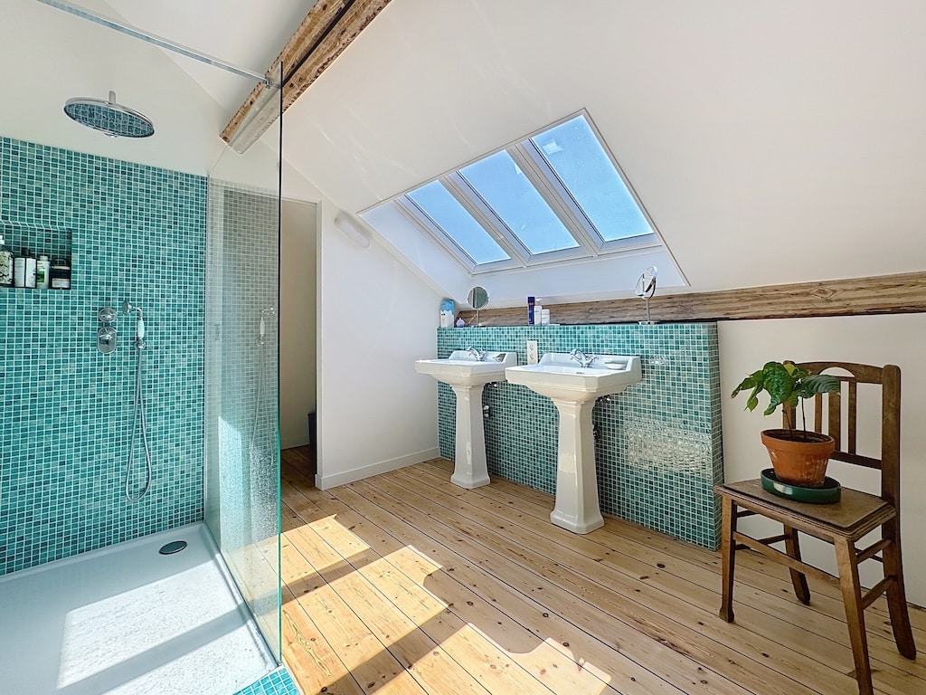 Salle de bain attique moderne avec murs turquoise, douche en verre et ambiance chaleureuse en bois.