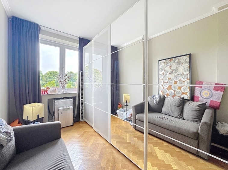 Salon moderne et cosy avec canapé gris, miroir, œuvre d’art géométrique et parquet en bois.