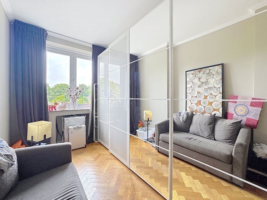 Salon moderne et cosy avec canapé gris, miroir, œuvre d’art géométrique et parquet en bois.