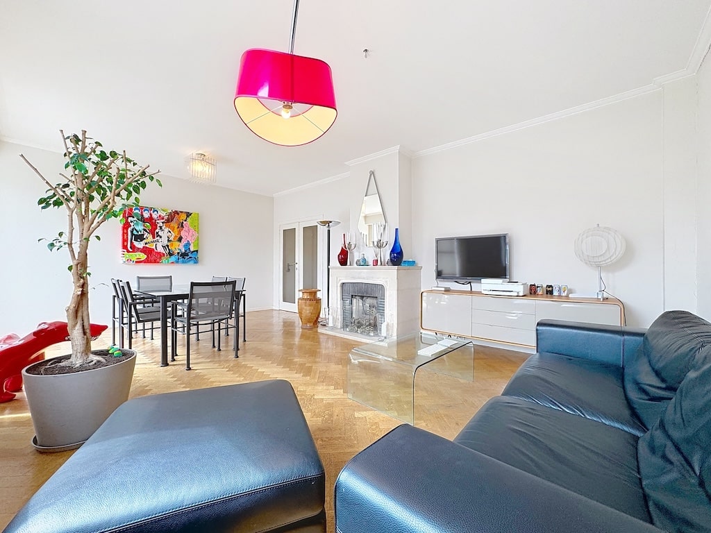 Salon moderne lumineux avec canapé bleu, cheminée décorative, espace repas et décoration colorée.
