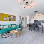 Salon contemporain avec canapé teal, déco colorée, espace repas moderne et cuisine blanche élégante.