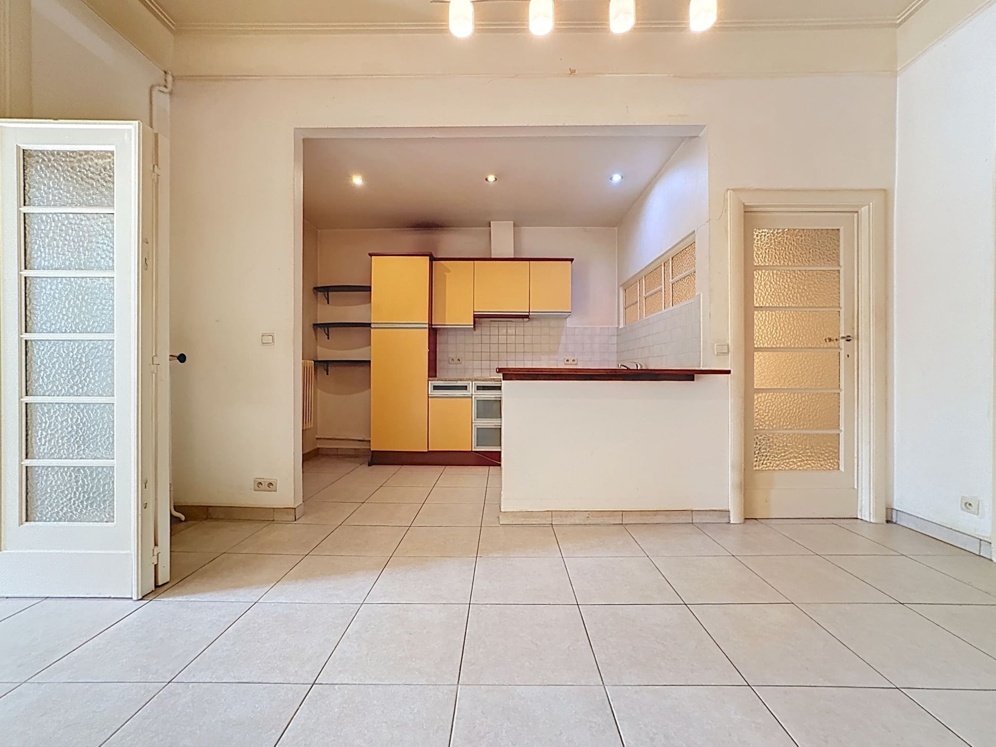Espace ouvert moderne avec cuisine jaune lumineuse, design minimaliste et grande luminosité naturelle.