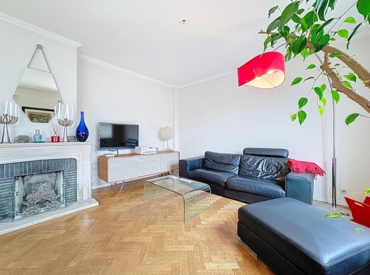 Salon moderne, chaleureux, lumineux, avec canapé en cuir, plante verte, mobilier élégant et touches rouges.