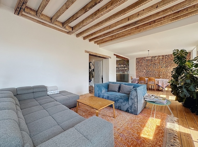 Salon moderne lumineux avec canapé gris, mur en briques, mobilier en bois et touche végétale.