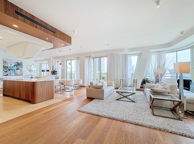 Salon contemporain lumineux avec cuisine élégante, mobilier neutre, grandes fenêtres et décor moderne.