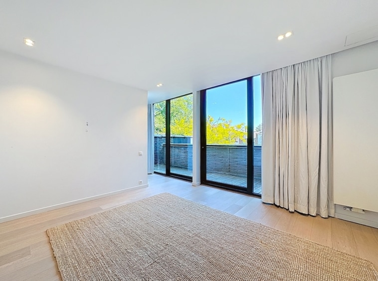 Salon lumineux avec grandes fenêtres, sol en bois clair, décoration minimaliste, vue sur l’extérieur.