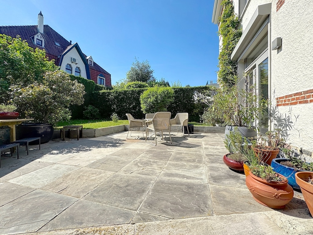 Terrasse cosy en pierre, mobilier en rotin, végétation luxuriante, ambiance chaleureuse et relaxante.