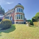 Villa de luxe avec dôme, jardins soignés, pelouses verdoyantes et arbres majestueux.
