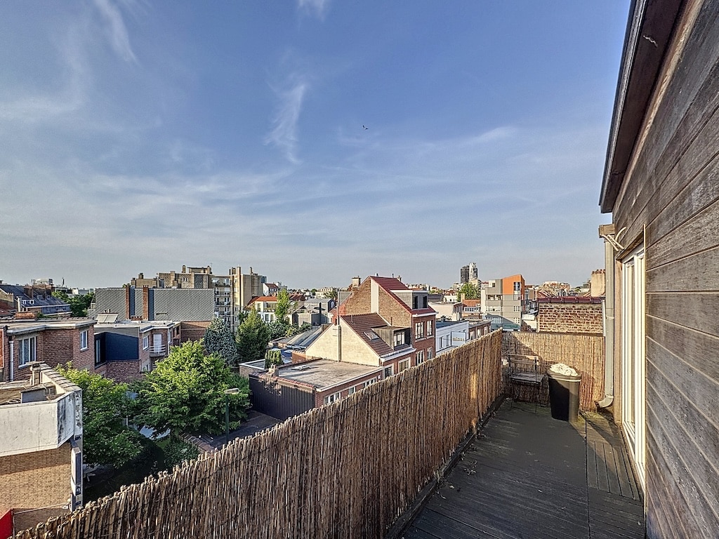 Balcon urbain avec vue sur toits, arbres et ciel clair, ambiance moderne et naturelle.