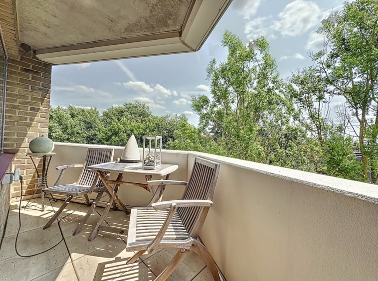 Balcon calme avec mobilier en bois, vue verte, table élégante, fleurs, bougie et ambiance relaxante.
