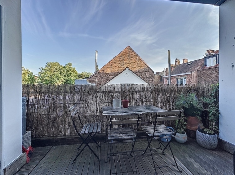 Balcon cosy avec table en bois, plantes, vue sur toits traditionnels en briques, ambiance relaxante.