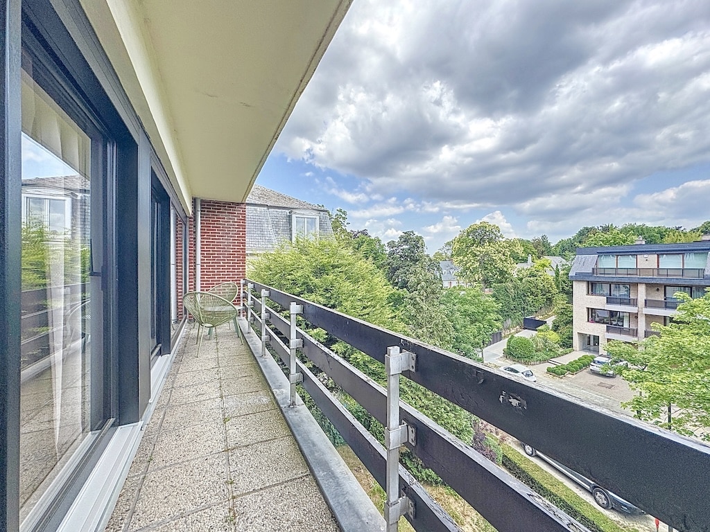 Balcon contemporain avec vue verdoyante, fauteuil minimaliste, ciel dramatique, parfait pour détente et contemplation.