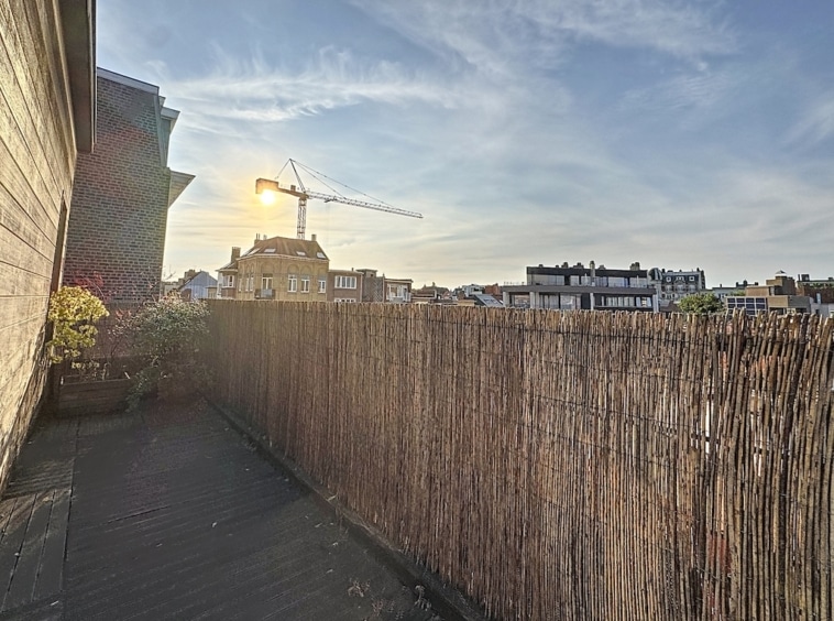 Balcon urbain au coucher du soleil avec plantes, vue sur la ville et construction en cours.