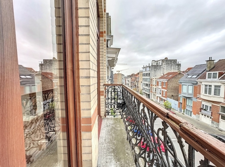 Balcon urbain avec rampe en fer forgé, vue sur bâtiments anciens et modernes sous ciel nuageux.