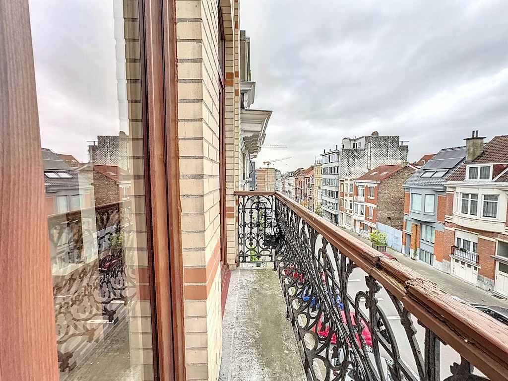 Balcon urbain avec rampe en fer forgé, vue sur bâtiments anciens et modernes sous ciel nuageux.