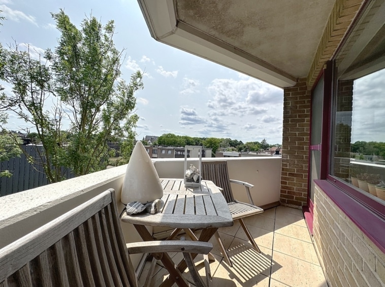 Balcon urbain paisible avec mobilier en bois, vue sur nature et ciel bleu en ville.