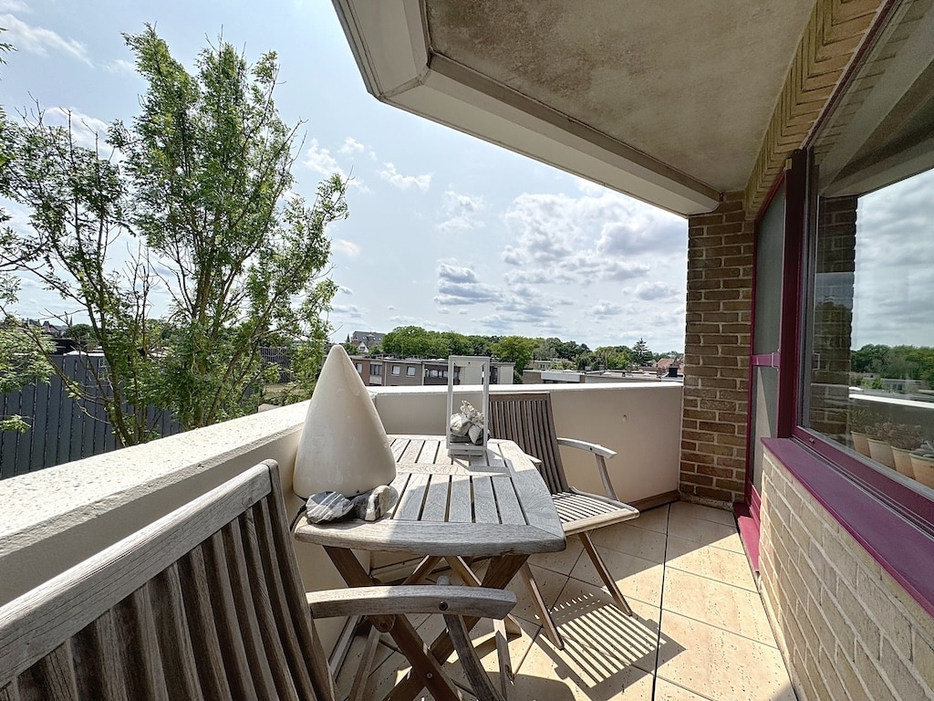 Balcon urbain paisible avec mobilier en bois, vue sur nature et ciel bleu en ville.