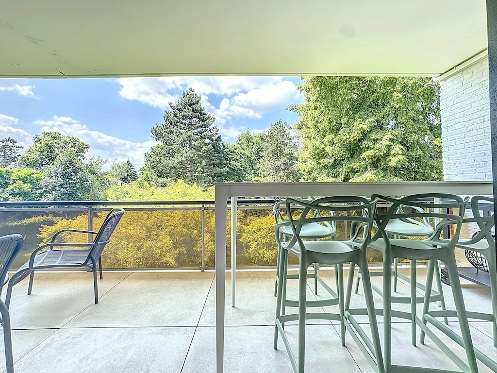 Balcon moderne avec vue sur nature, mobilier minimaliste, ciel ensoleillé, parfait pour détente et repas.