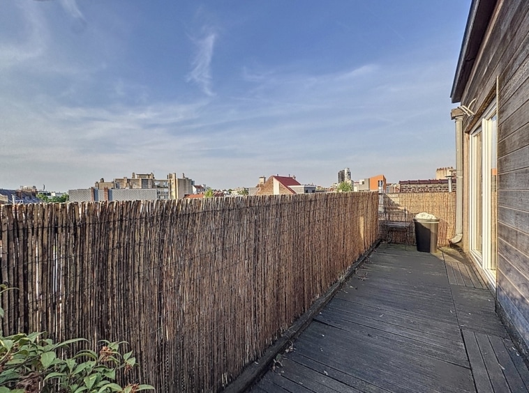 Balcon en bois avec vue urbaine, clôture en bambou, lumière naturelle et espace détente.