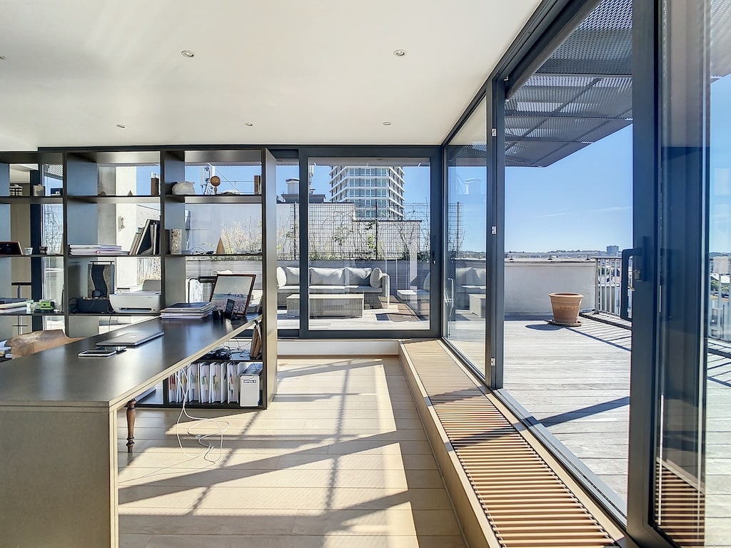 Espace de travail moderne avec vue lumineuse, terrasse extérieure et mobilier épuré.