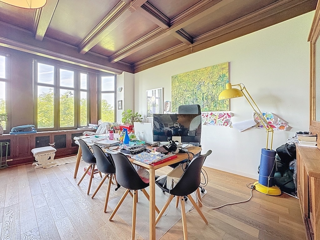 Bureau lumineux avec poutres en bois, grandes fenêtres, décoration colorée et ambiance chaleureuse.