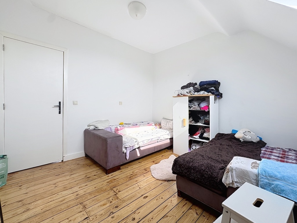 Chambre lumineuse minimaliste avec lits pastel, sol en bois et grande fenêtre naturelle.