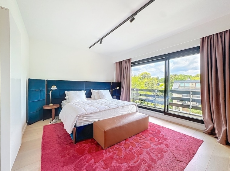 Chambre moderne lumineuse avec lit bleu, tapis rouge, fenêtre panoramique et décoration épurée.
