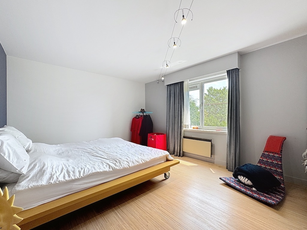 Chambre minimaliste lumineuse avec lit en bois, vue sur la nature, détails colorés et mobilier moderne.