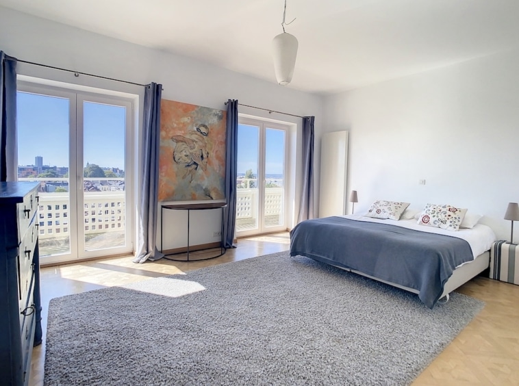 Chambre moderne lumineuse avec grandes fenêtres, mobilier minimaliste et décoration artistique élégante.
