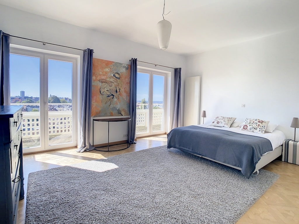 Chambre moderne lumineuse avec grandes fenêtres, mobilier minimaliste et décoration artistique élégante.