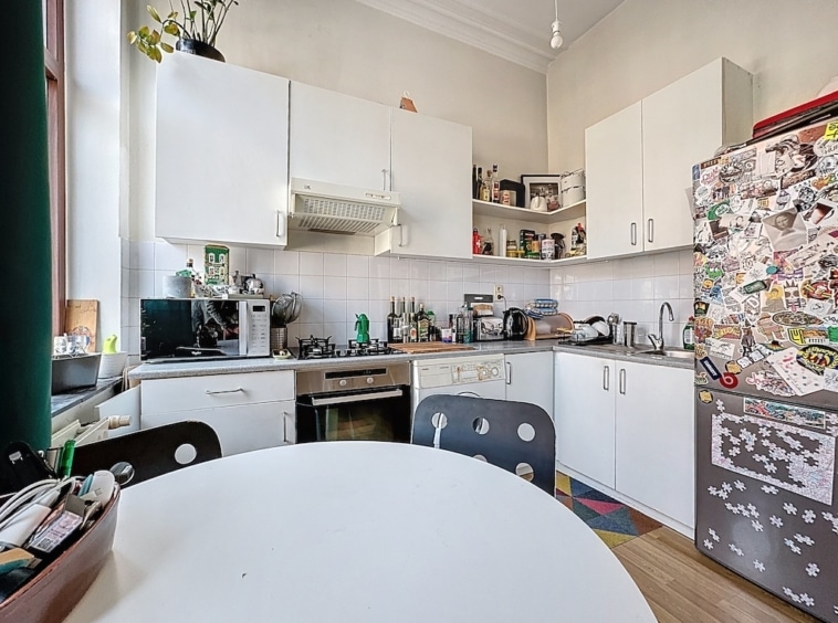 Cuisine lumineuse et conviviale avec mobilier blanc, table ronde, appareils pratiques et décor éclectique.